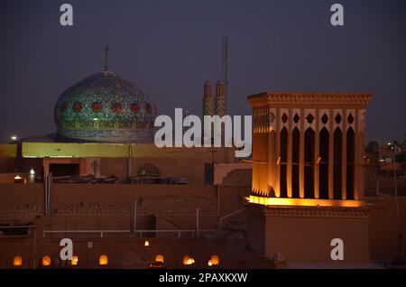 Beleuchteter Windturm und farbenfrohe Kuppel einer Moschee in Yazd, Iran im Abendlicht Stockfoto