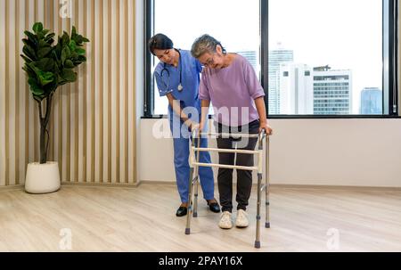 Eine Physiotherapeutin in blauer Uniform hilft älteren Menschen, sich zu bewegen und das Gehen auf Gehhilfe oder Gehstock zu üben. Gesundheits- und Medizinkonzept. Stockfoto