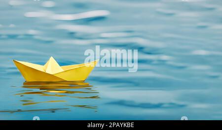 Ein einziges gelbes Papierboot auf blauem Wasser - symbolisch für abenteuerliche Zukunftsperspektiven Stockfoto