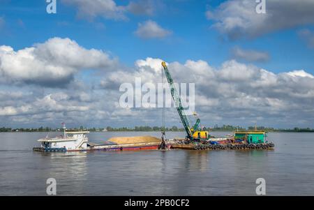 Ein schwimmender Bagger auf dem Mekong in der Provinz Kandal, Kambodscha, der Sand und Zuschlagstoffe aus dem Flussbett zieht und sie in einem Kahn entsorgt. Stockfoto