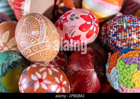 Nahaufnahme von oben. Die Ostereier sind zufällig dicht nebeneinander gestapelt und bilden eine farbenfrohe Osterkomposition, während sie den gesamten Rahmen eng ausfüllen. Stockfoto