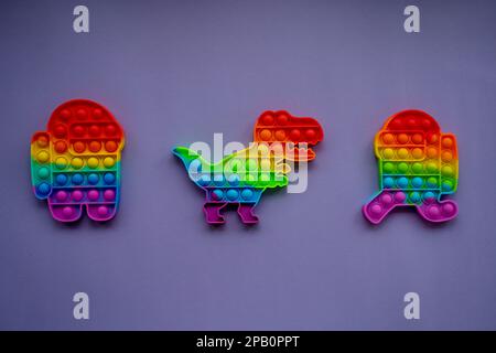 Trendige Pop-it-und einfache Grübchen-Spielzeuge in Form von Dinosauriern, und eine Figur unter uns mit sehr hohem Hintergrund Stockfoto