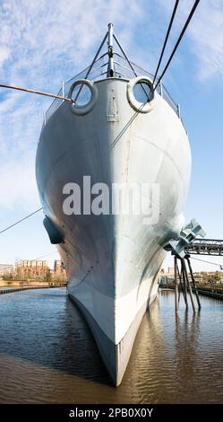 Das Schlachtschiff USS North Carolina hat in Wilmington, NC, angelegt. Vollständige Sicht auf den Bug des Schiffs von der Küste aus mit Verankerungsseilen. Volle Sonne, blauer Himmel Stockfoto