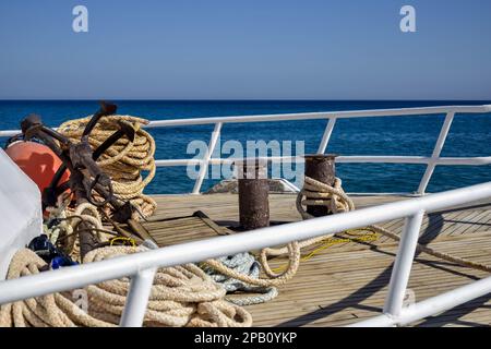 Bug der weißen Yacht auf dem Hintergrund des blauen Meeres. Dickes Ankerseil ist um die Poller gewickelt. Stahlgeländer-Zäune. Draufsicht. Nahaufnahme. Stockfoto