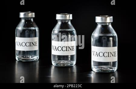 Drei Glasfläschchen mit Impfstoff auf schwarzem Brett, Nahaufnahme Stockfoto