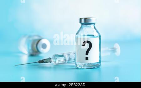 Impfstoffflasche mit Injektionsnadel in der Nähe, Fragezeichen auf dem Etikett, ein weiteres verschwommenes Fläschchen mit blauem Hintergrund Stockfoto