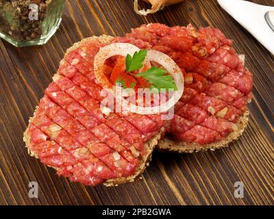Scharfes Fleisch aus Rinderfarm auf einer Brötchen mit Zwiebeln auf Holzgrund Stockfoto
