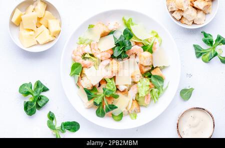 Caesar Salat mit Garnelen, Eisberg und Lammsalat, Croutons, Parmesan mit caesar Dressing. Weißer Tischhintergrund, Draufsicht Stockfoto