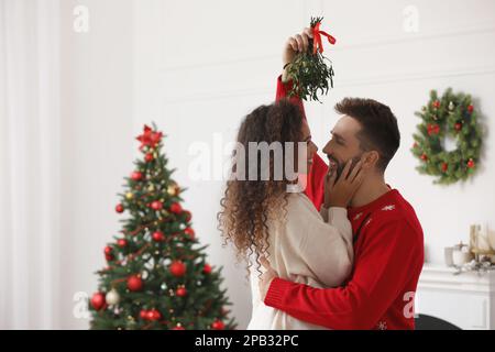 Ein reizendes Paar unter Mistelzweigen im Zimmer, das zu Weihnachten dekoriert war Stockfoto