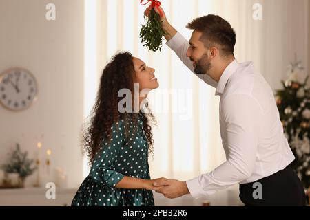 Ein reizendes Paar unter Mistelzweigen im Zimmer, das zu Weihnachten dekoriert war Stockfoto