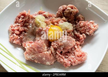 Hackfleisch, Ei, Zwiebeln und Gewürze in einer Schüssel. Zubereitung von zerkleinerten Koteletts in Polen, traditionelle polnische Kotlettmielone. Stockfoto