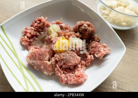 Hackfleisch, Ei, Zwiebeln und Gewürze in einer Schüssel. Zubereitung von zerkleinerten Koteletts in Polen, traditionelle polnische Kotlettmielone. Rolle in Milch getaucht in Bg. Stockfoto