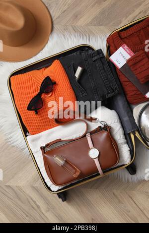 Offener Koffer mit gefalteter Kleidung und Accessoires auf dem Boden, flach liegend Stockfoto