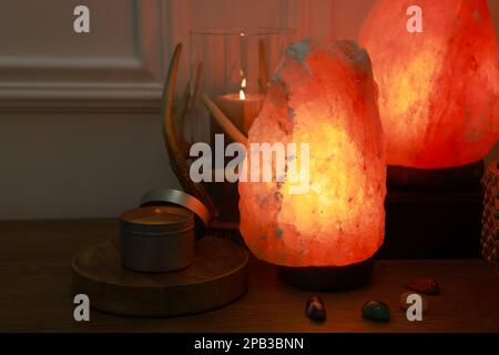 Salzlampen, Kerzen und Edelsteine des Himalaya auf einem Holztisch in der Nähe weißer Innenwände Stockfoto