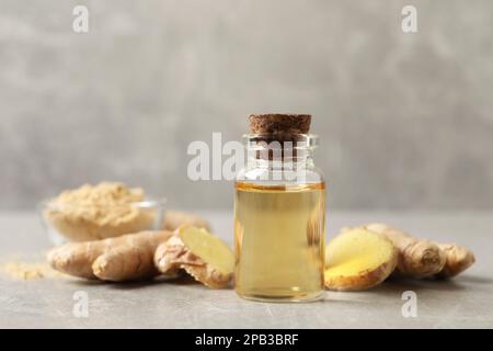 Glasflasche mit ätherischem Öl und Ingwerwurzel auf grauem Tisch Stockfoto