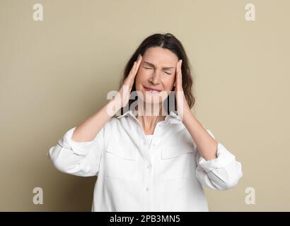 Reife Frau mit Kopfschmerzen auf beigefarbenem Hintergrund Stockfoto