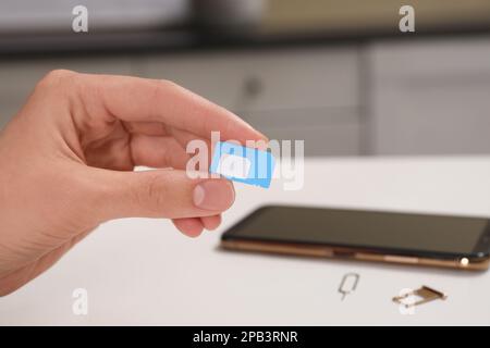 Frau mit SIM-Karte am weißen Tisch im Haus, Nahaufnahme Stockfoto