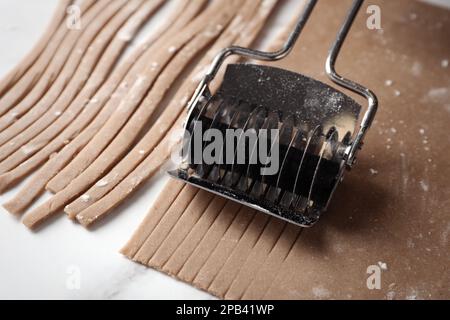 Soba (Buchweizennudeln) mit Schneidevorrichtung am weißen Marmortisch, Nahaufnahme Stockfoto