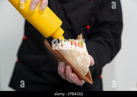 Der Koch gießt weiße Tzatziki-Sauce auf einen Pita-kreta-Snack im Fast-Food-Restaurant. Traditionelle griechische Fast-Food-Küche Stockfoto