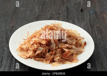 Katsuobushi getrocknete Bonito-Flocken oder auf einer weißen Keramikplatte auf Holzhintergrund. Stockfoto