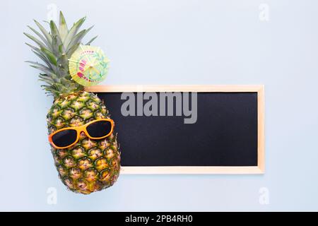 Ananas in Sonnenbrille mit leerer Tafel für Ihren Text auf blauem Hintergrund Stockfoto