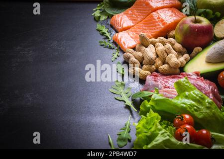 Frisches Gemüse, Obst, Fisch, Fleisch, Nüsse auf schwarzem Kreidetafel. " Auliflower, Avocado, Äpfel, Tomaten, Lachs, Rindfleisch, Spinat, Kräuter. Diät Stockfoto