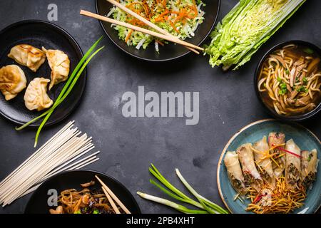 Chinesisches Essen mit dunklem Hintergrund. Chinesische Nudeln, gebratener Reis, Nudelsuppe, Dim Sum, Frühlingsrollen, Salat. Traditionelle chinesische Gerichte. Leertaste für Stockfoto