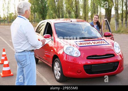 Frau, die im Freien aus dem Auto aussteigen konnte, in der Nähe eines Senior-Instruktors. Bestandener Führerschein-Test Stockfoto