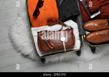 Offener Koffer mit gefalteter Kleidung, Accessoires und Schuhen auf dem Boden, Draufsicht Stockfoto