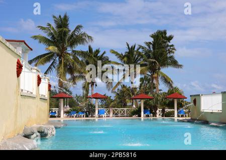 Blick auf Swimmingpool und Sonnenschirme mit leeren Liegestühlen vor Palmen. Urlaub am Strand Resort auf tropischer Insel Stockfoto