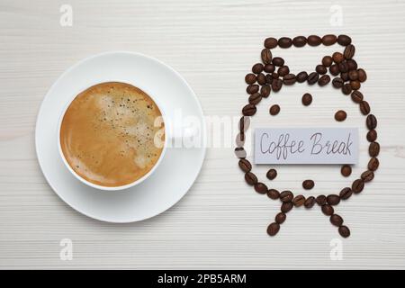 Wecker aus Bohnen und Karte mit Phrase Kaffeepause neben heißem Getränk auf weißem Holztisch, flach liegend Stockfoto