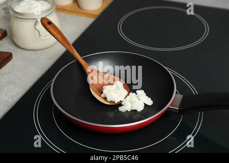 Bratpfanne mit Kokosnussöl und Holzspachtel auf Induktionsofen. Gesundes Kochen Stockfoto