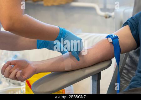 Eine Krankenschwester in blauen Handschuhen führt eine Nadel ein, um Blut zu entnehmen. Blutspende Stockfoto