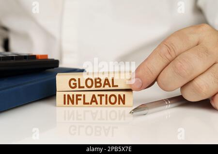 Geschäftskonzept. In den Händen eines Geschäftsmannes, Holzblöcke mit der Aufschrift "Globale Inflation", neben einem Notizbuch und einem Taschenrechner. Stockfoto