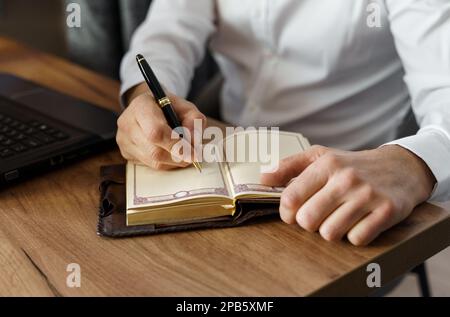 Ein Geschäftsmann sitzt an einem Tisch und macht Notizen in einem Notizbuch. Nahaufnahme. Stockfoto