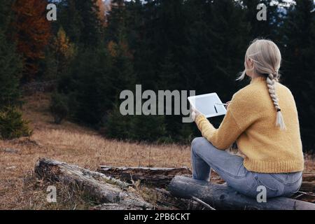 Junge Frau, die im Herbst im Wald mit einem Grafiktablett malt Stockfoto