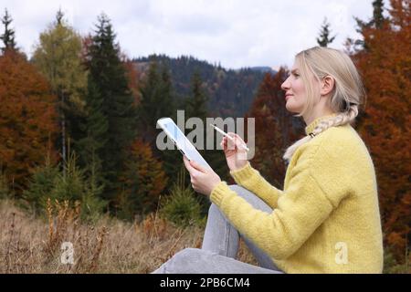 Junge Frau, die am Herbsttag mit einem Grafiktablett in den Bergen malt Stockfoto