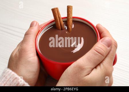 Eine Frau, die eine Tasse leckere heiße Schokolade mit Zimt auf hellem Hintergrund hält, Nahaufnahme Stockfoto