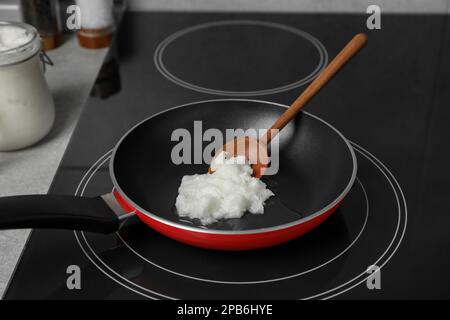 Bratpfanne mit Kokosnussöl und Holzspachtel auf Induktionsofen. Gesundes Kochen Stockfoto