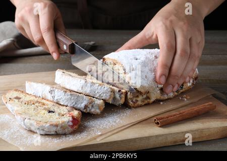 Frau schneidet traditionelle Weihnachtsstollen auf Holzbrett, Nahaufnahme Stockfoto