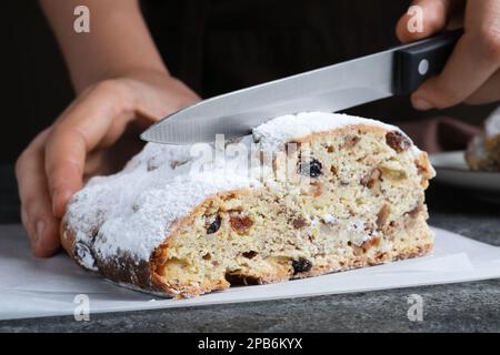 Frau schneidet traditionelle Weihnachtsstollen am grauen Tisch, Nahaufnahme Stockfoto