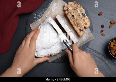 Frau schneidet traditionellen Weihnachtsstollen am schwarzen Tisch, Draufsicht Stockfoto