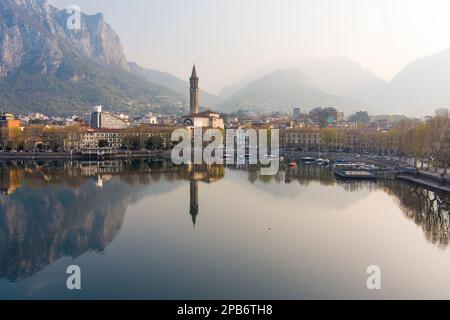 Neblige Sonnenaufgang-Stadtlandschaft von Lecco am Frühlingstag. Malerische Uferpromenade der Stadt Lecco zwischen dem berühmten Comer See und dem malerischen Bergamo A. Stockfoto