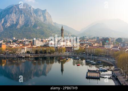 Neblige Sonnenaufgang-Stadtlandschaft von Lecco am Frühlingstag. Malerische Uferpromenade der Stadt Lecco zwischen dem berühmten Comer See und dem malerischen Bergamo A. Stockfoto