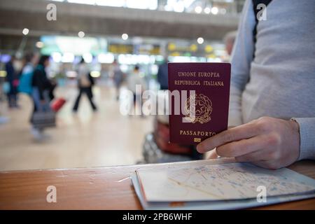 Nahaufnahme eines italienischen Passes, der von einem Reisenden gehalten wird, mit einer Karte daneben. Stockfoto