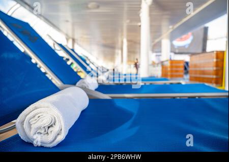 Ein gerolltes Handtuch auf einem Liegestuhl in einer Reihe auf einem Kreuzfahrtschiff Deck. Stockfoto