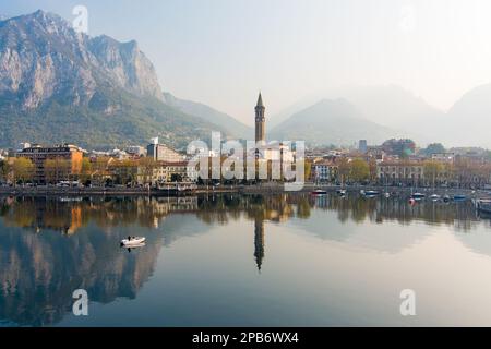 Neblige Sonnenaufgang-Stadtlandschaft von Lecco am Frühlingstag. Malerische Uferpromenade der Stadt Lecco zwischen dem berühmten Comer See und dem malerischen Bergamo A. Stockfoto