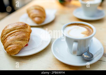 Zwei Tassen Cappuccino-Kaffee mit Croissants auf einem Holztisch. Kaffee am Morgen im Café im Freien. Stockfoto