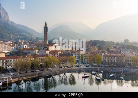 Neblige Sonnenaufgang-Stadtlandschaft von Lecco am Frühlingstag. Malerische Uferpromenade der Stadt Lecco zwischen dem berühmten Comer See und dem malerischen Bergamo A. Stockfoto