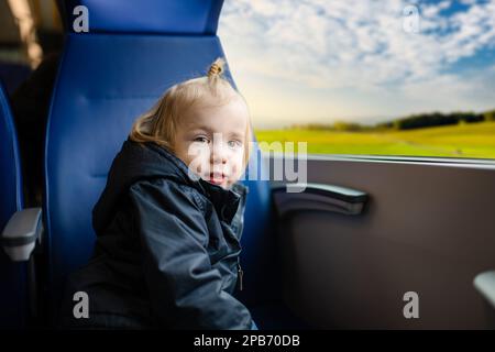 Kleiner Junge, der mit dem Zug reist. Ein kleines Kind, das im Expresszug am Fenster sitzt, während des Familienurlaubs. Kind in einem Eisenbahnwaggon. Ich fahre mit in den Urlaub Stockfoto
